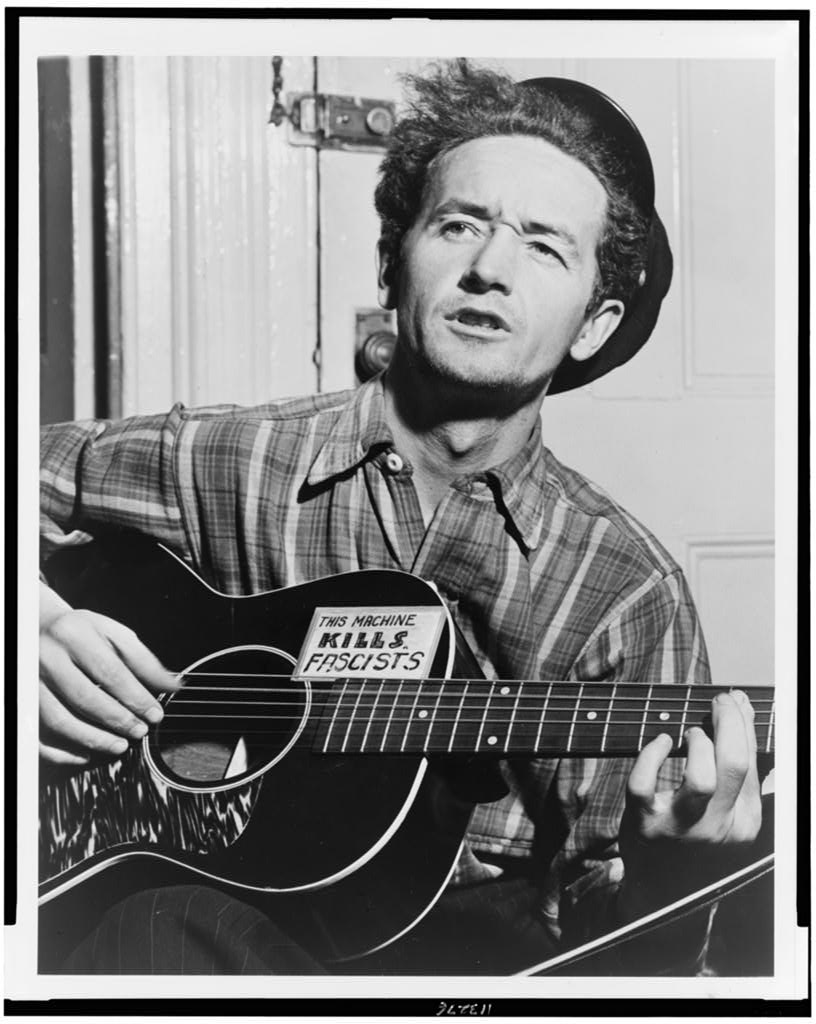 Woody Guthrie, half-length portrait, facing slightly left, holding guitar] / World Telegram photo by Al Aumuller (1943). Courtesy of Library of Congress.